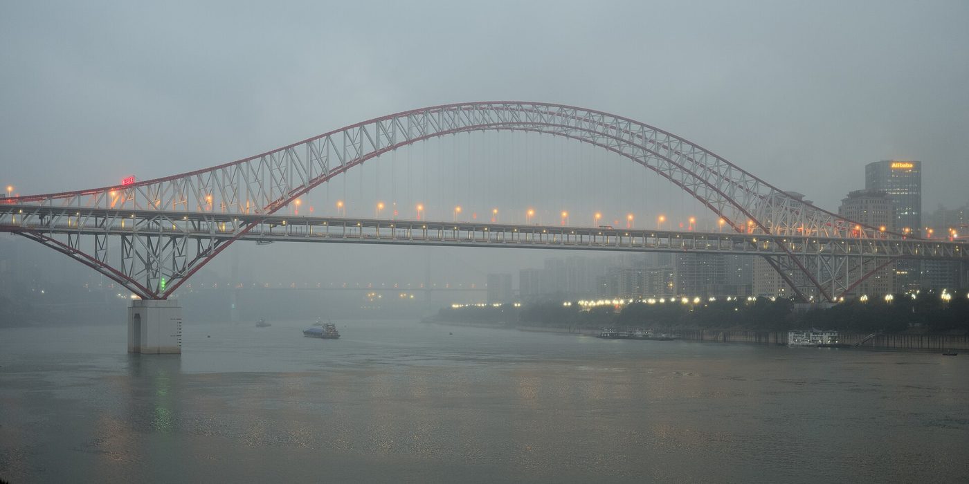 The Chaotianmen steel arch bridge over the Yangtze River in Chongqing at dusk, its lights visible through winter fog.